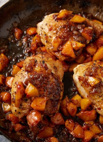 A skillet with three pieces of seasoned, cooked chicken and peaches, topped with a glossy, chunky peach sauce and surrounded by diced peaches.