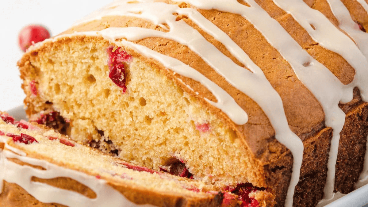 A sliced loaf of cranberry bread with a golden crust, dotted with cranberries, and drizzled with white icing on top.