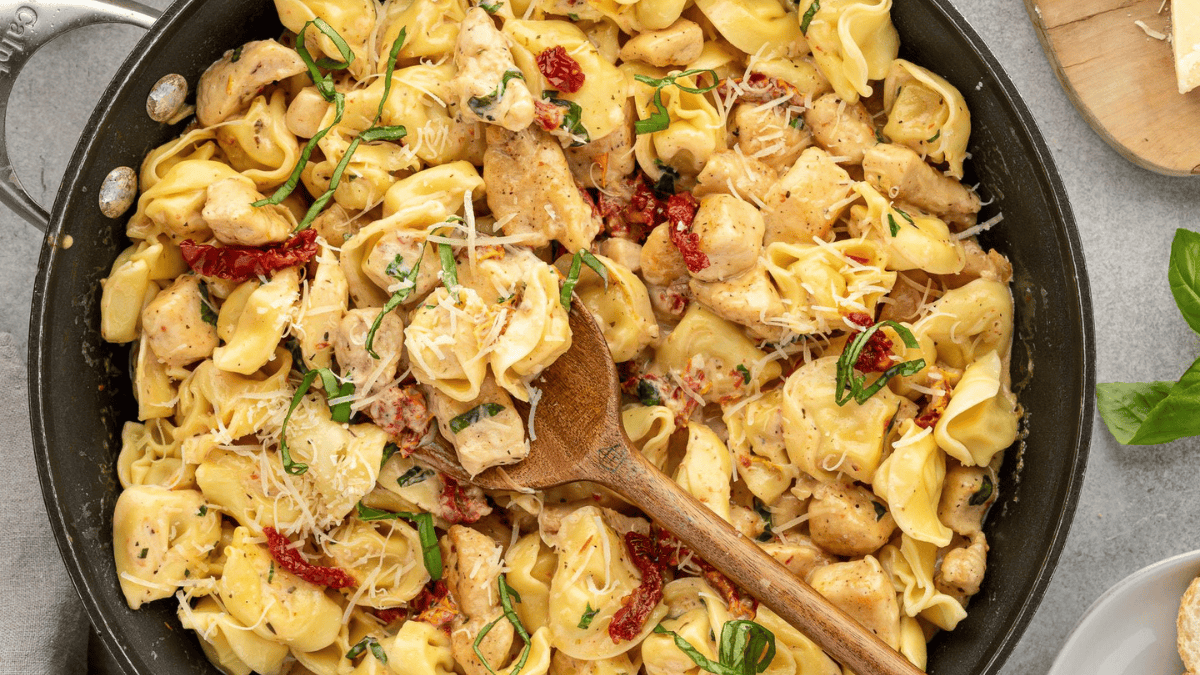 A skillet filled with creamy tortellini pasta, chicken, sun-dried tomatoes, and basil, topped with shredded cheese. It’s one of those weeknight dinners that hit the table in 30 minutes or less—a comforting meal made simple.