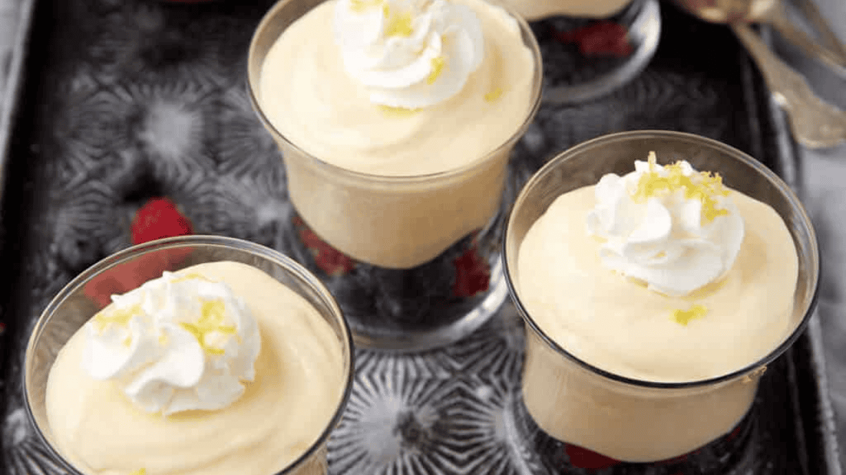 Three glass cups filled with mousse topped with whipped cream and lemon zest, sitting on a tray, with berries visible at the bottom of each glass.
