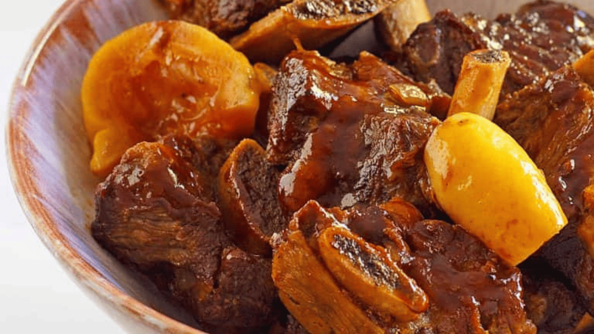 A bowl filled with braised beef short ribs in a rich, glossy sauce, garnished with slices of cooked yellow lemon.