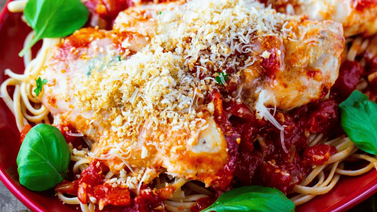 A plate of spaghetti topped with breaded chicken, tomato sauce, grated cheese, and fresh basil leaves.