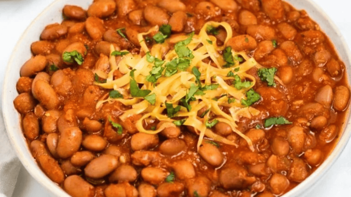 A bowl filled with chili beans in a rich tomato sauce, topped with shredded cheese and chopped fresh cilantro.