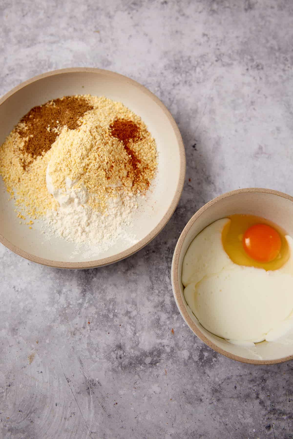 Two bowls on a gray countertop: one holds flour, breadcrumbs, and spices—the perfect coating for Southern Fried Pickles—while the other contains cream and a raw egg yolk.