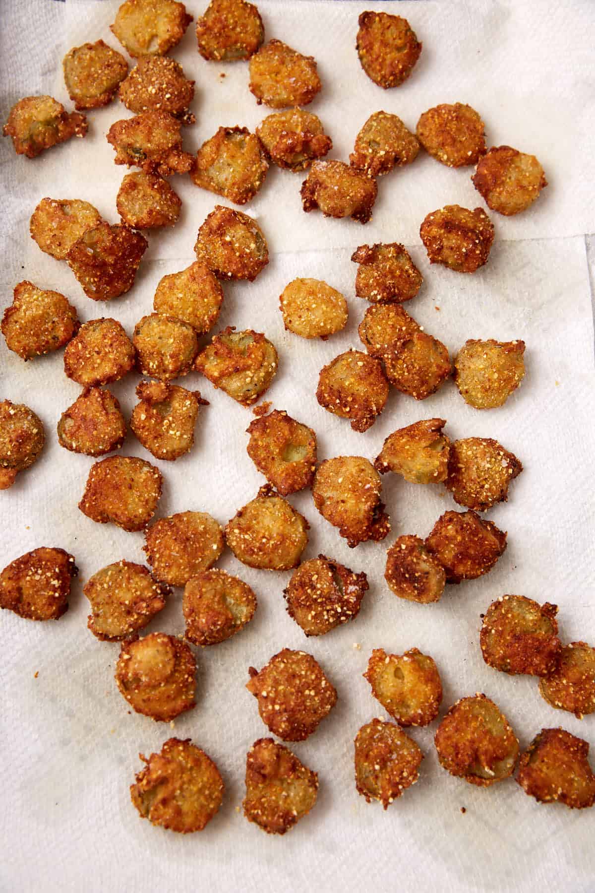 Golden brown, crispy Southern Fried Pickles are spread out on white paper towels, likely to absorb excess oil after frying.