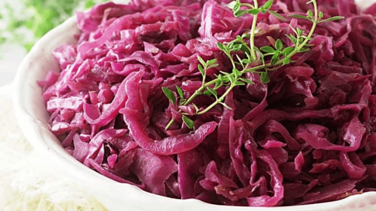 A white bowl filled with cooked red cabbage garnished with fresh green thyme sprigs.