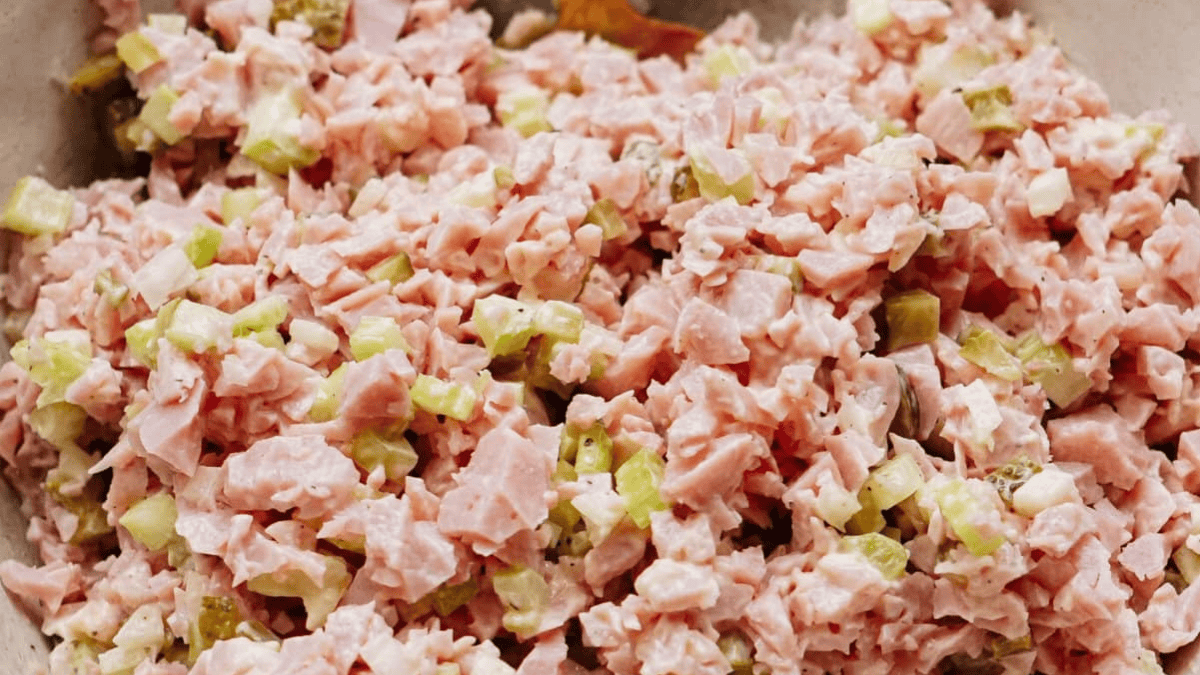 A close-up of a creamy ham salad mixture with diced ham, celery, and pickles, all finely chopped and blended together.