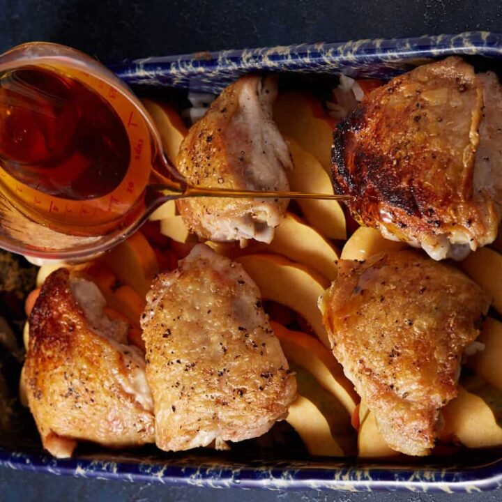 Maple syrup being poured over chicken thighs in a baking dish.