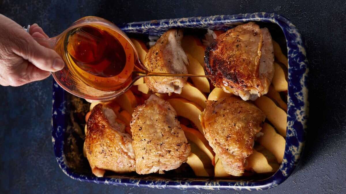 Maple syrup being poured over chicken thighs in a baking dish.