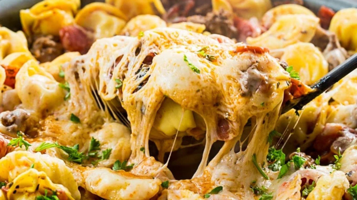 Cheesy tortellini pasta bake with browned cheese, ground meat, herbs, and tomato sauce, with a fork lifting a gooey, cheesy portion from the dish.