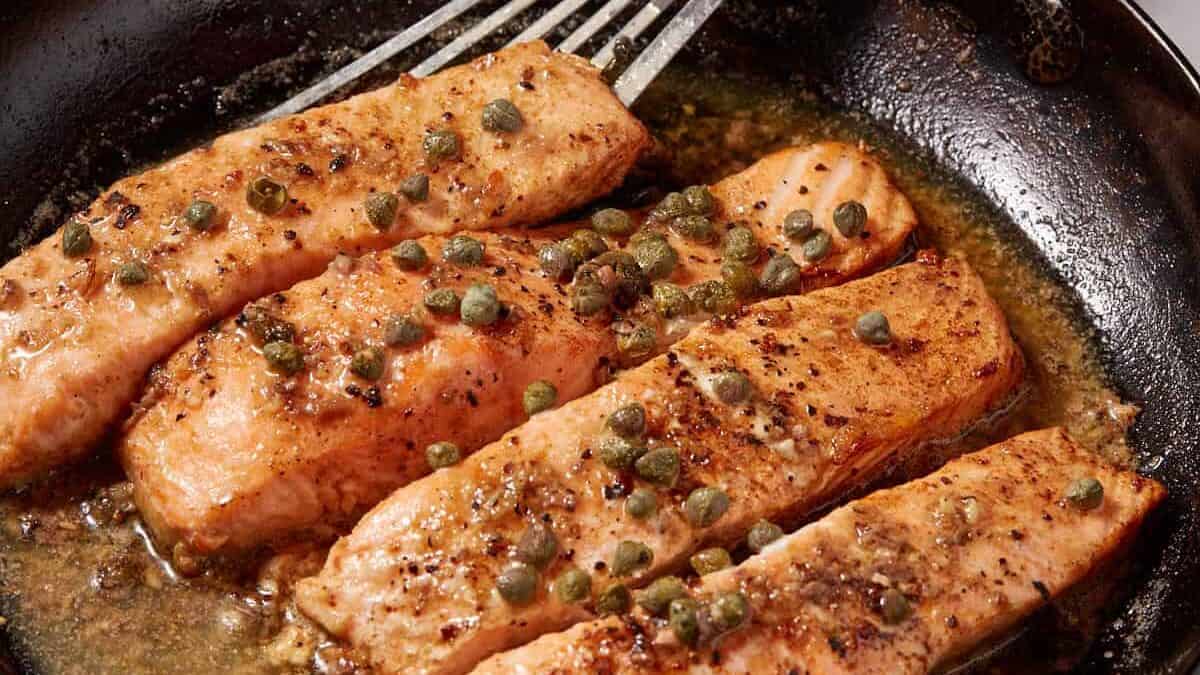 A skillet of salmon fillets with a spatula and a lemon.