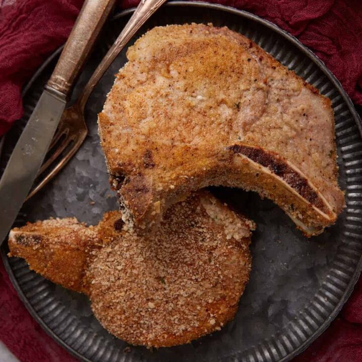 Two pork chops on a plate with a knife and fork.