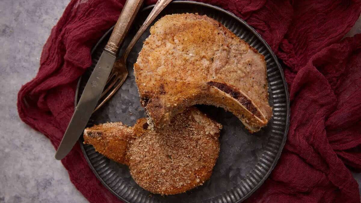 Two pork chops on a plate with a knife and fork.