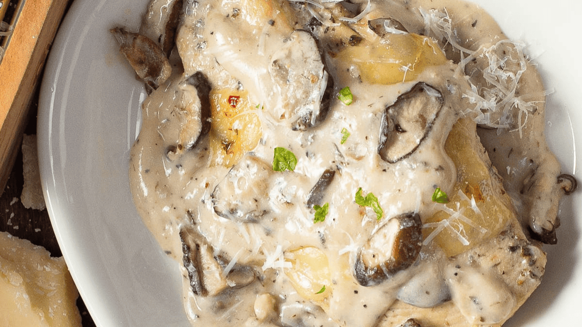 A close-up of creamy mushroom sauce over pasta, garnished with grated cheese and fresh herbs, served in a white bowl.