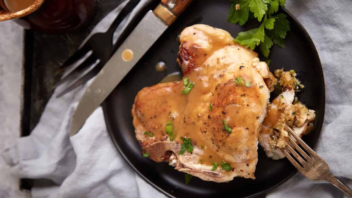 A stuffed pork chop on a plate covered in gravy.