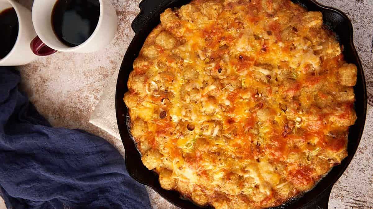 A skillet of potato sausage casserole next to coffee cups.