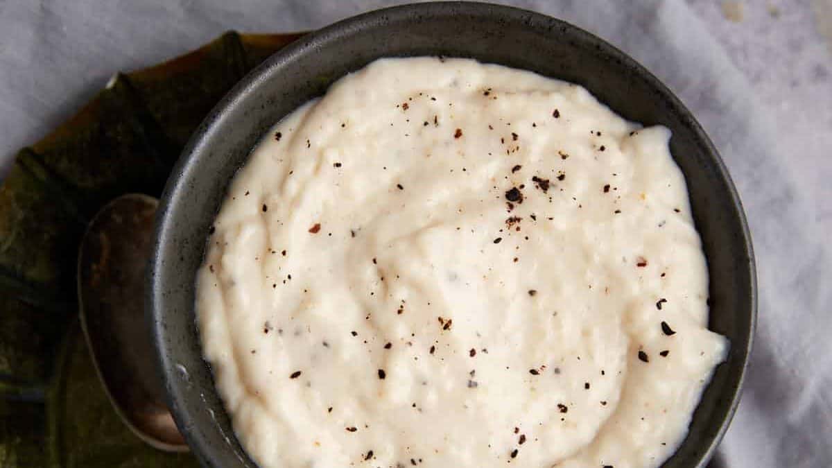 A bowl of white gravy with a spoon next to it.