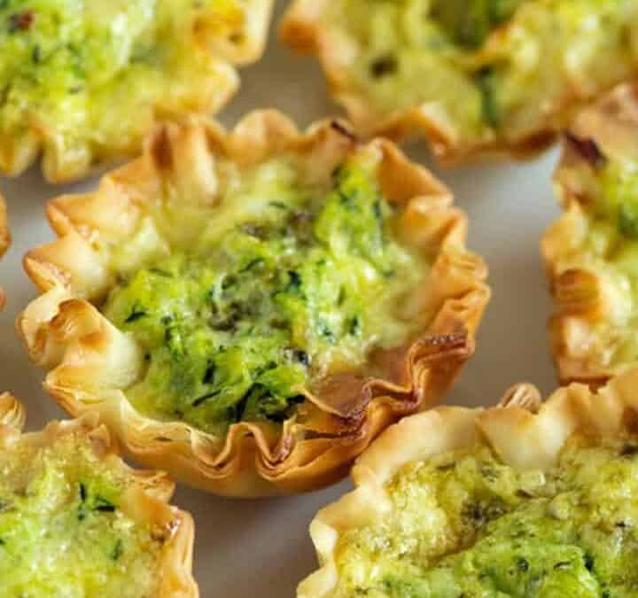 A platter of zucchini quiches with basil leaves.