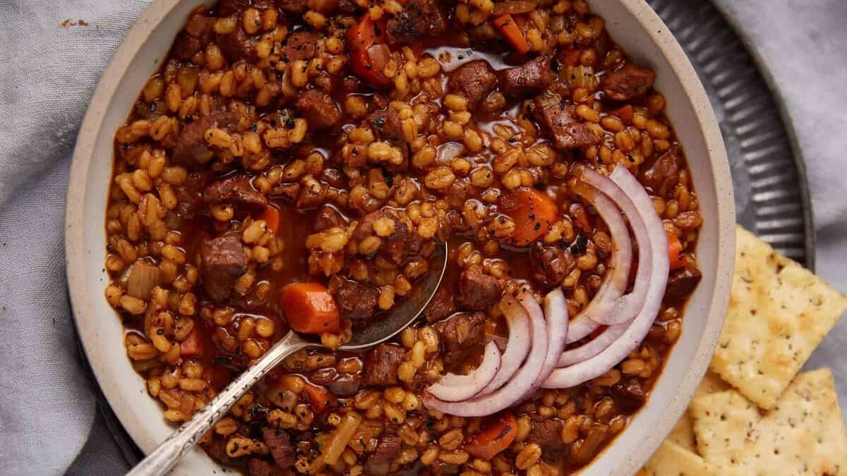 A bowl of beef and barley stew with sliced onions on top.