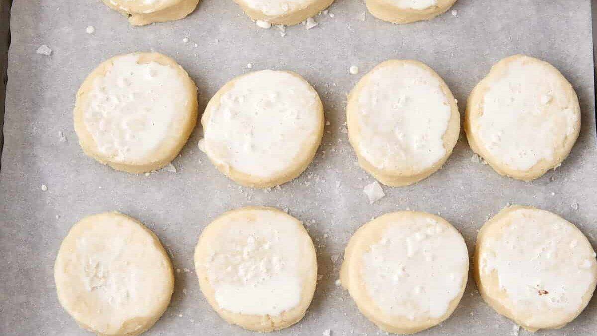 Biscuits brushed with cream on a baking tray.