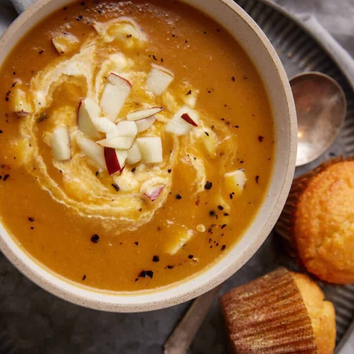 Apple and butternut squash soup with a swirl of sour cream next to corn muffins.