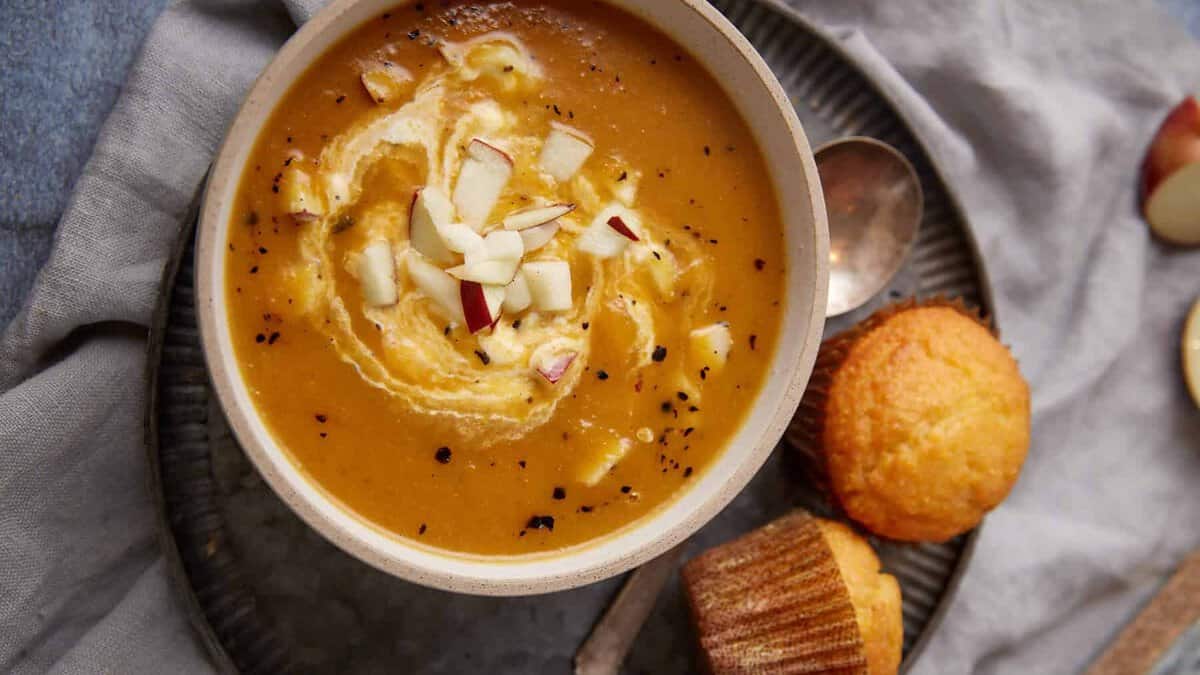 Apple and butternut squash soup with a swirl of sour cream next to corn muffins.