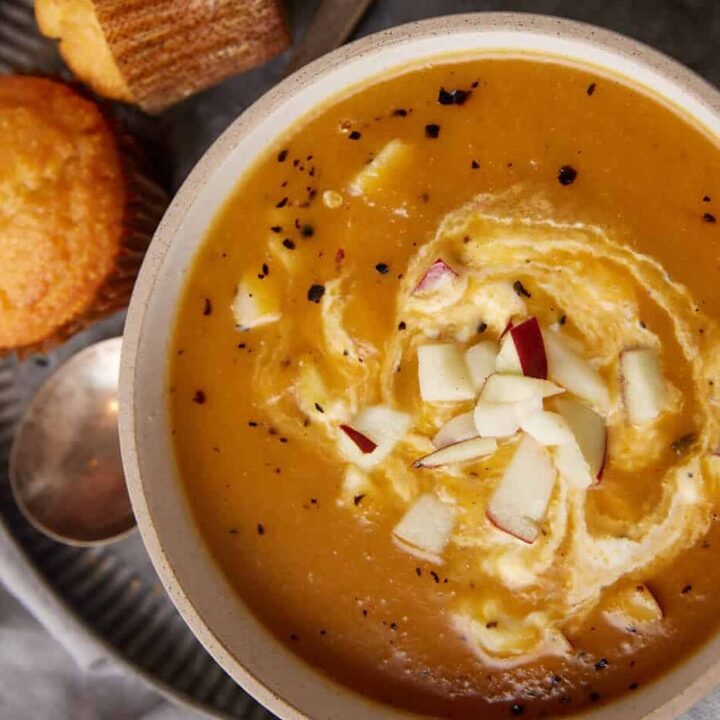 Apple and butternut squash soup with a swirl of sour cream next to corn muffins.