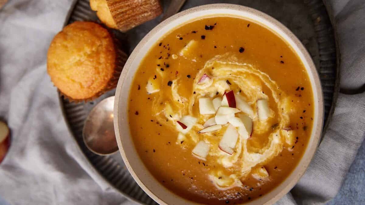 Apple and butternut squash soup with a swirl of sour cream next to corn muffins.