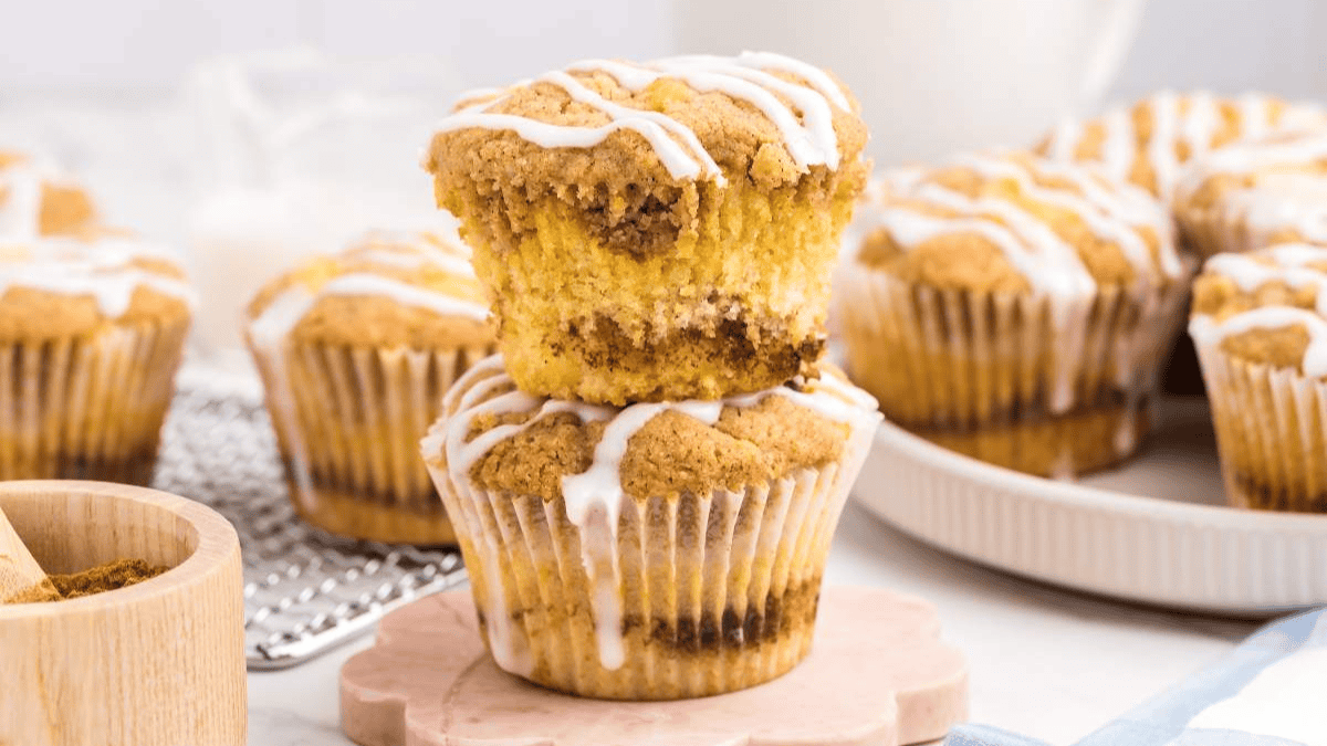 Two cinnamon streusel muffins, one stacked on top of the other, topped with white icing. More muffins are in the background alongside a bowl of brown sugar&mdash;perfect for pairing with creative coffee recipes beyond the mug.