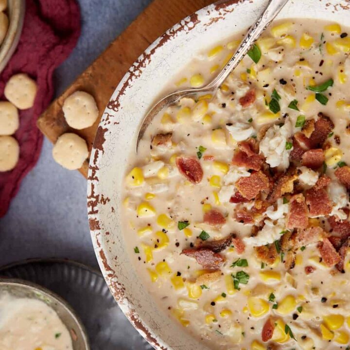 A bowl of corn and crab bisque next to a ladel and crackers.