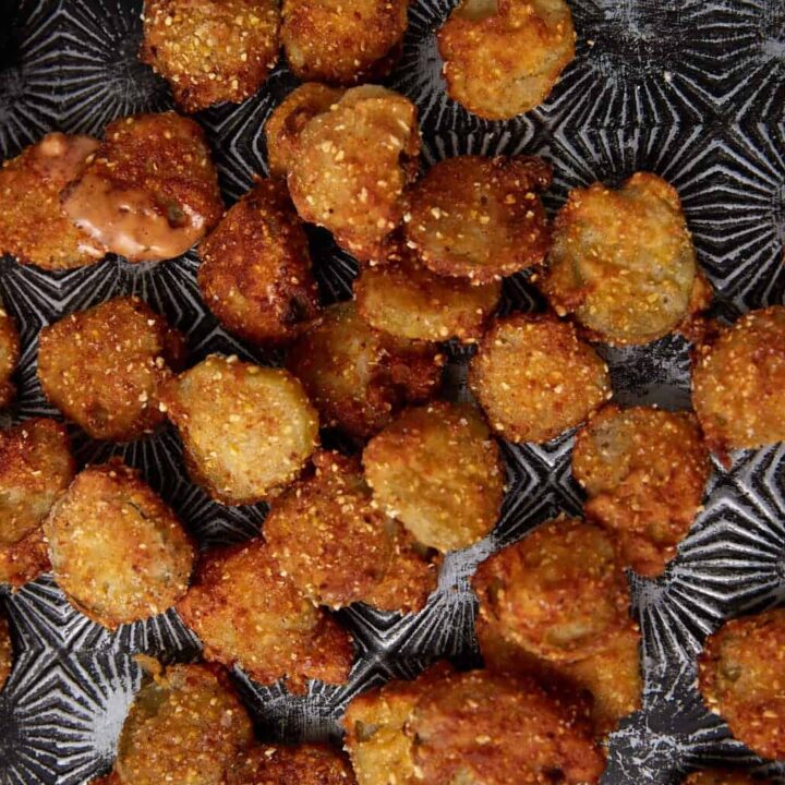 A batch of golden-brown Southern Fried Pickles is scattered on a dark textured tray, with a small bowl of creamy dipping sauce in the corner.