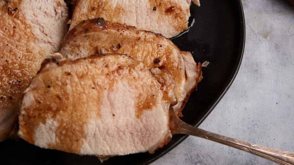 A serving fork removing a slice of pork roast. from a platter.