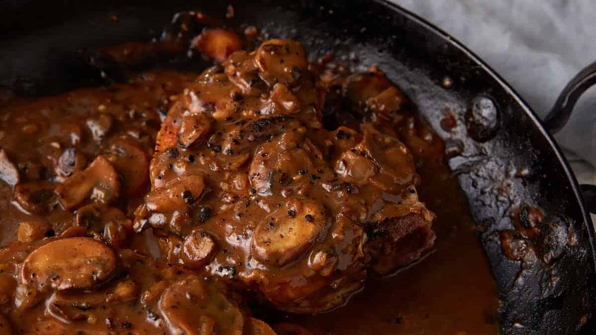 Pork chops in a skillet covered with gravy.