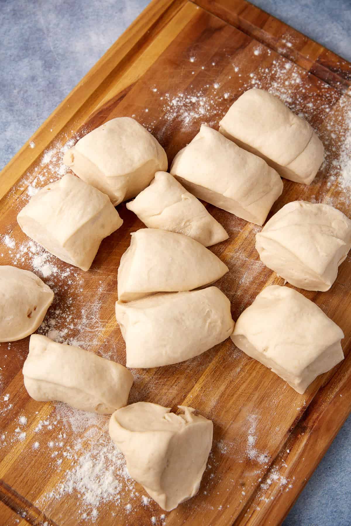 Several pieces of raw dough, soon to become soft pretzels, are cut into chunks and placed on a floured wooden board, ready for further preparation.
