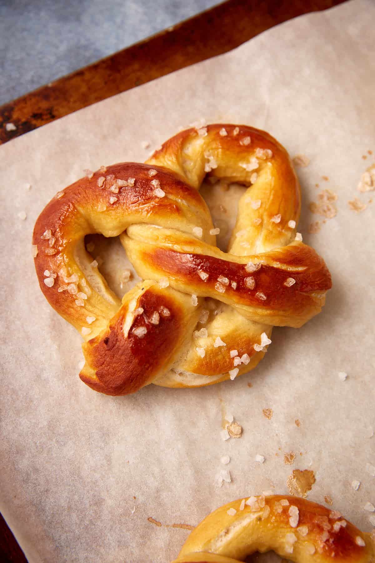 A freshly baked soft pretzel with a golden-brown crust and coarse salt sprinkled on top, resting on a sheet of parchment paper—perfect for lovers of classic soft pretzels.
