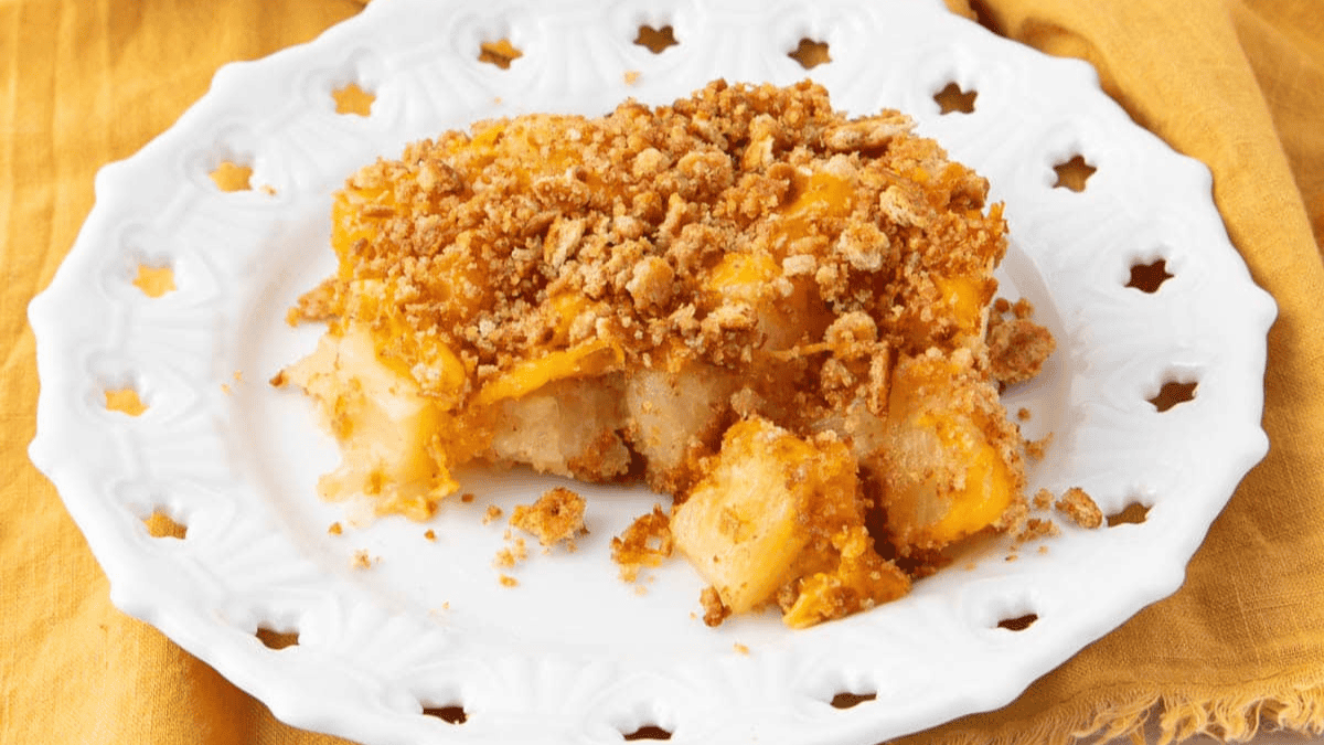 A serving of apple crisp with a crumbly oat topping sits on a white decorative plate, placed on a yellow cloth background.