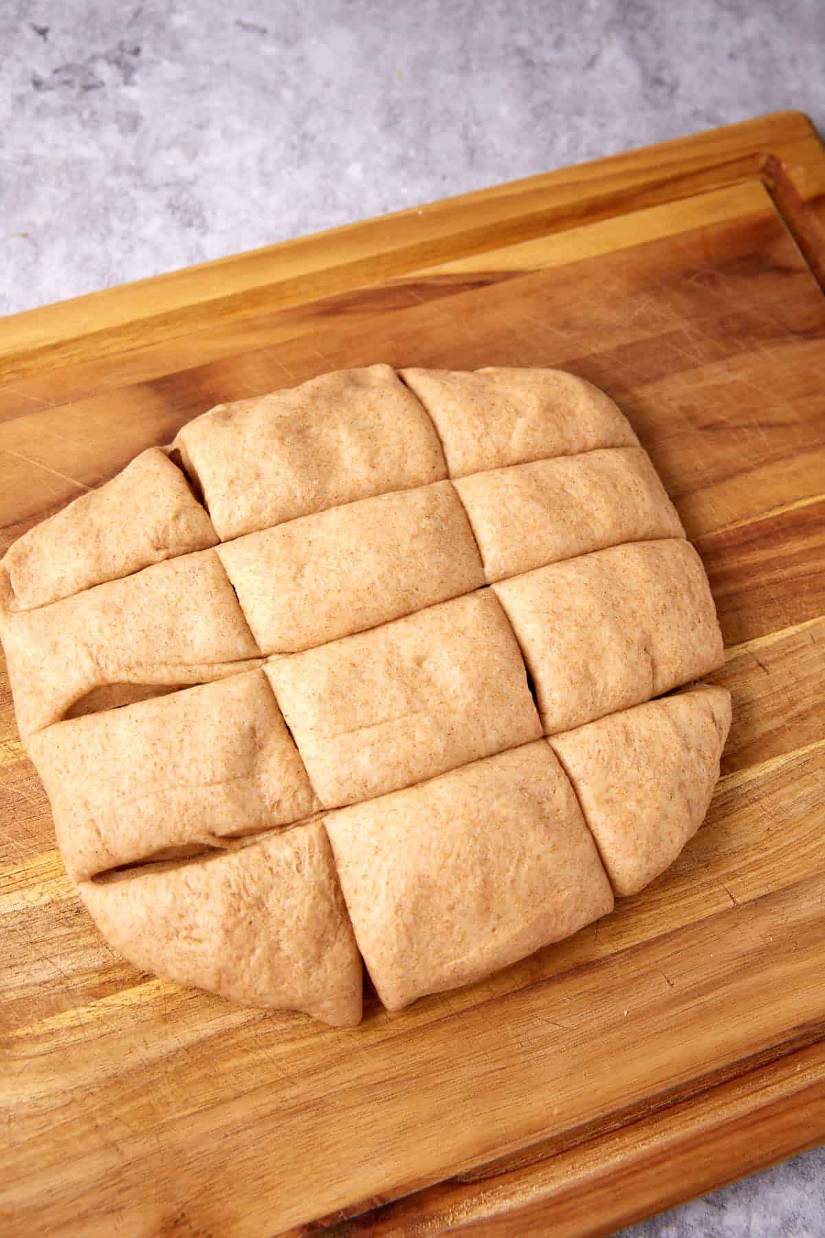 A slab of whole wheat dough, destined to become delicious whole wheat rolls, is cut into nine rectangular pieces on a wooden cutting board, ready for baking.