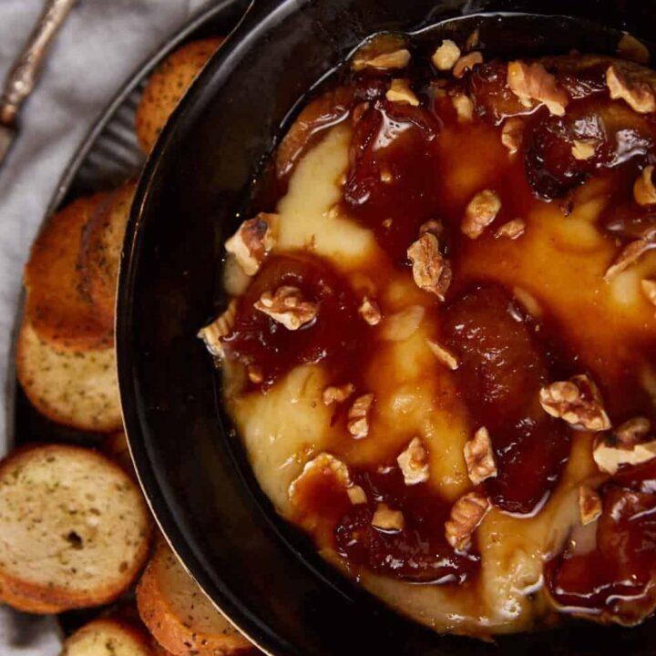 A dish of baked brie with apples next to crostini.