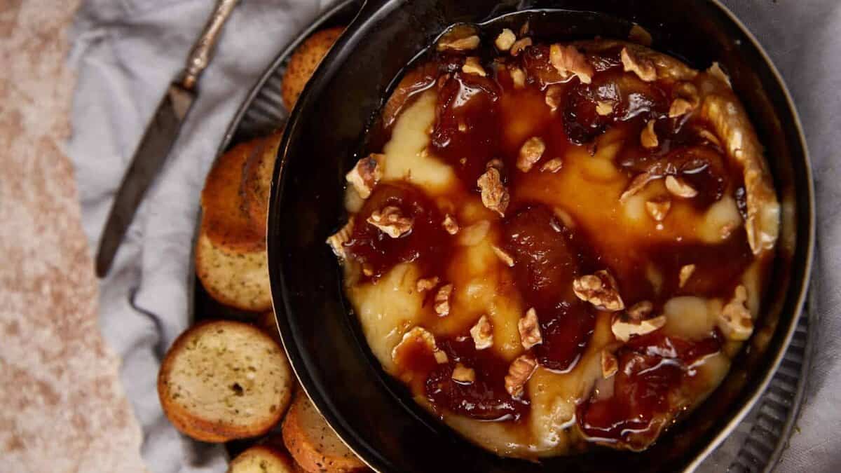 A dish of baked brie with apples next to crostini.