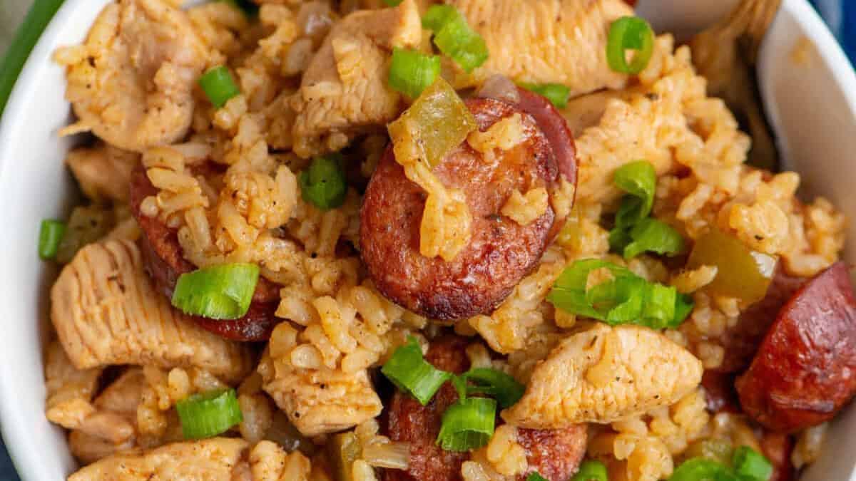 A close-up of a bowl filled with jambalaya, showing pieces of sausage, chunks of chicken, seasoned rice, and sliced green onions on top.