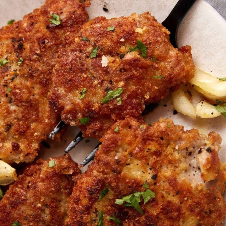 A serving fork removing a pork cutlet from a platter.