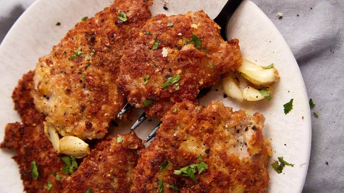 A serving fork removing a pork cutlet from a platter.