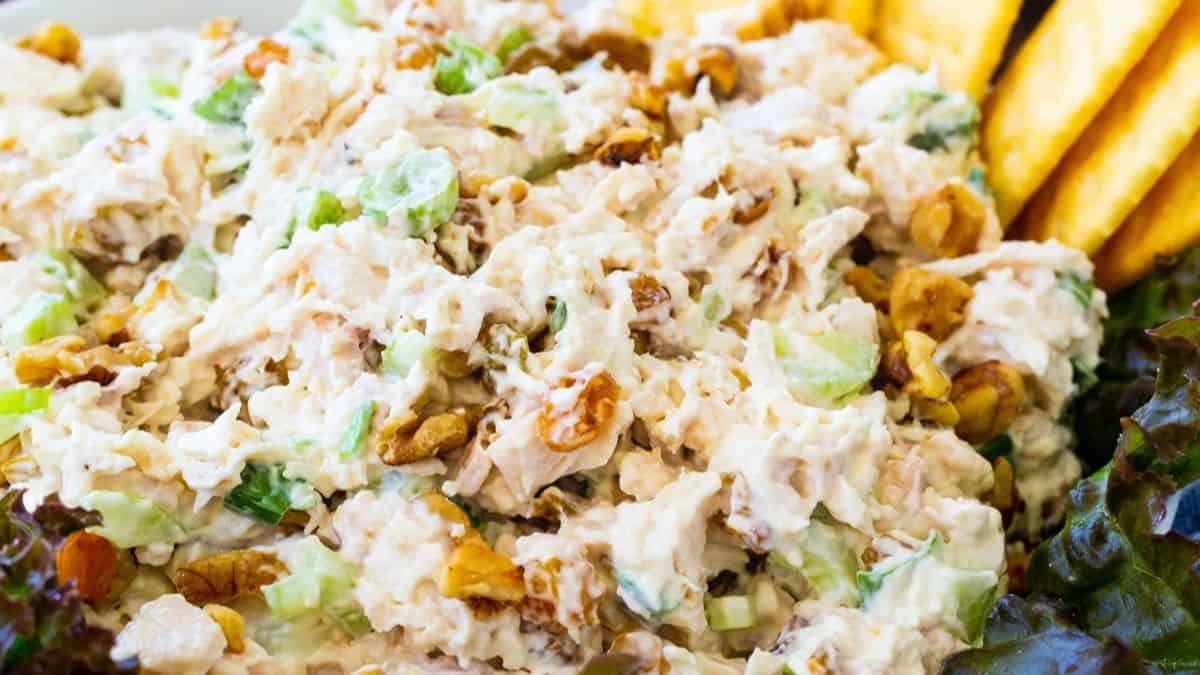 A close-up of chicken salad—one of those things Americans call salad that aren't salad—mixed with chopped celery, walnuts, and mayonnaise, served with leafy greens and crackers on the side.