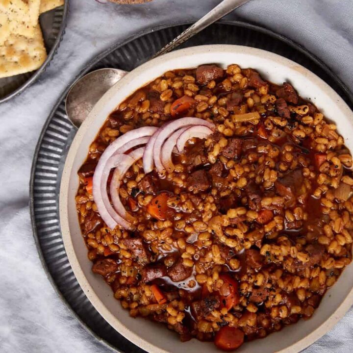 Beef and barley soup next to a plate of crackers.