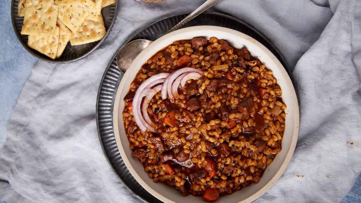 Beef and barley soup next to a plate of crackers.