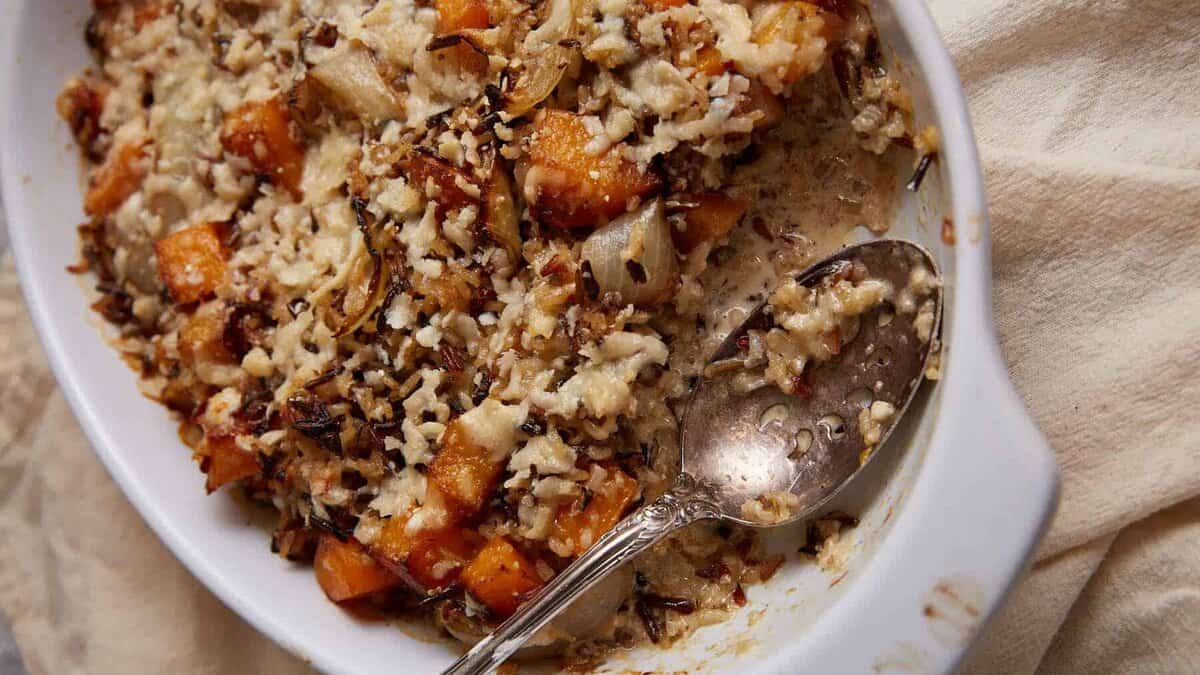 A serving spoon in a baking dish of butternut squash casserole.