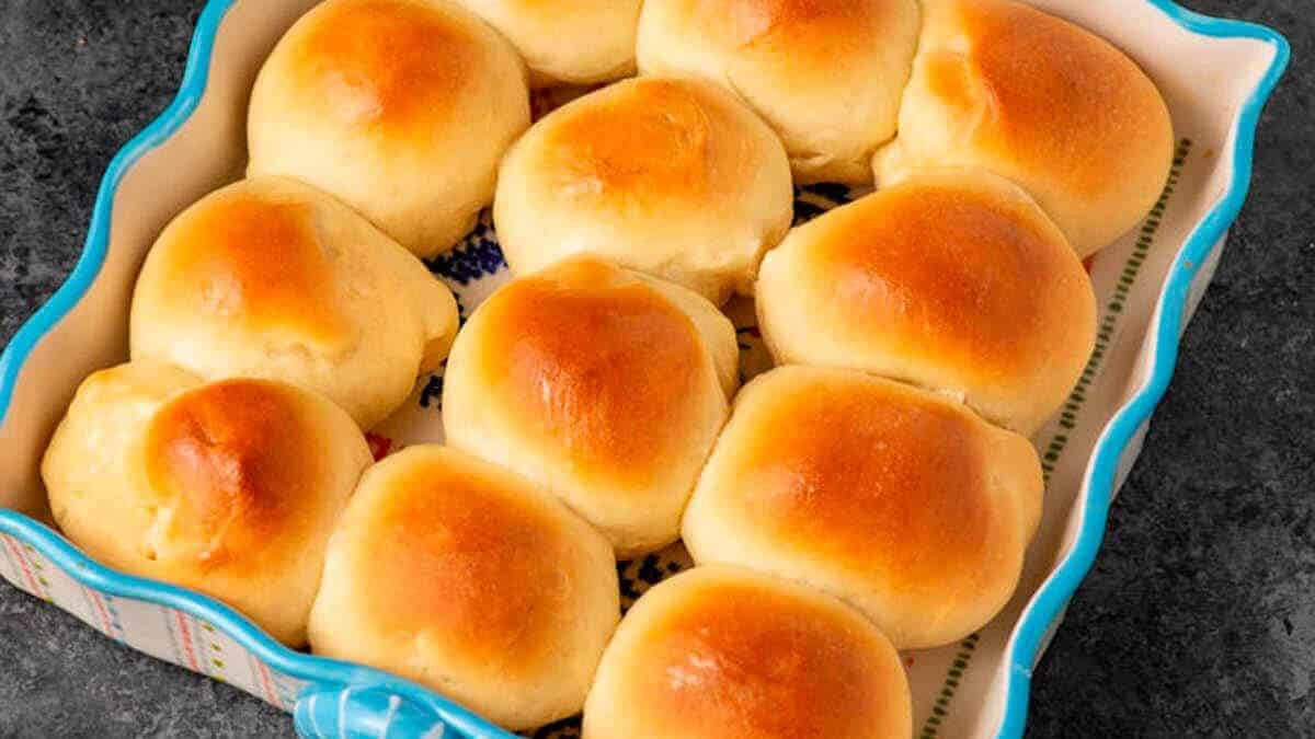 A baking dish filled with twelve golden-brown, fluffy dinner rolls arranged closely together on a dark countertop.
