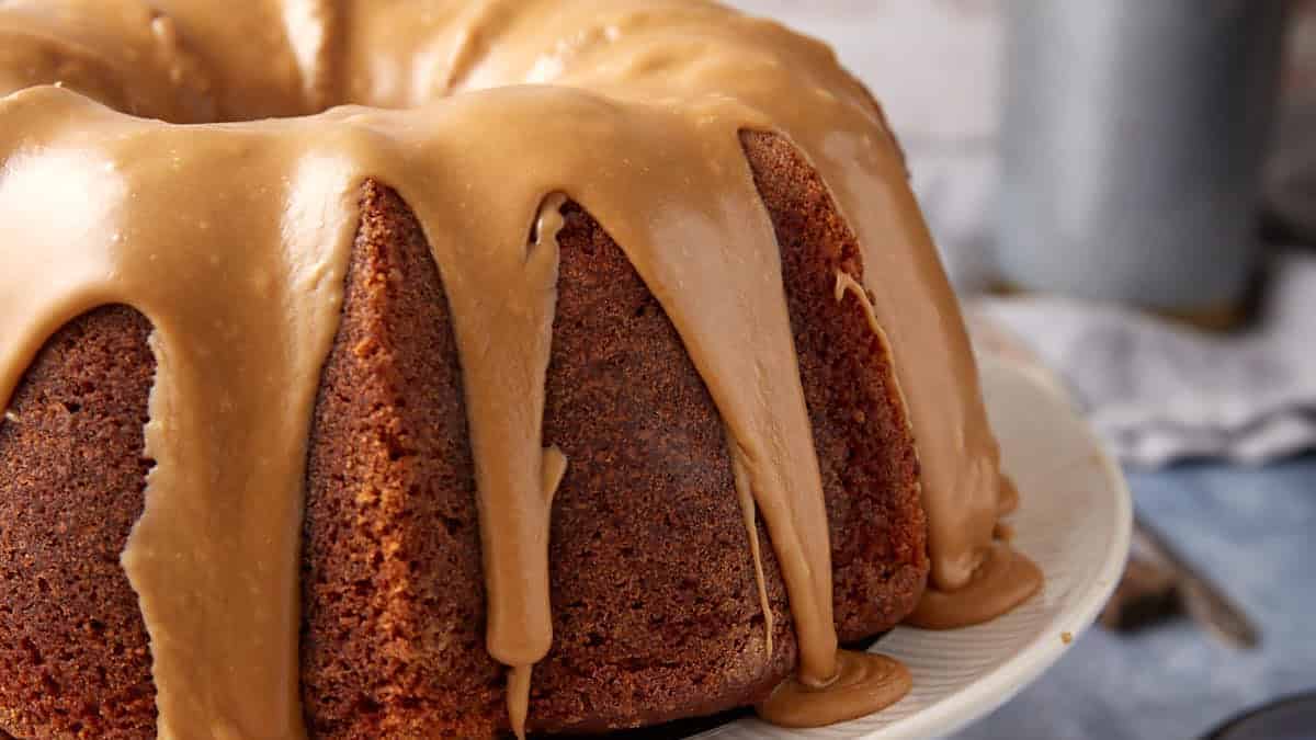 A close-up of a Bundt cake with light brown caramel or maple glaze dripping down the sides, displayed on a white plate.
