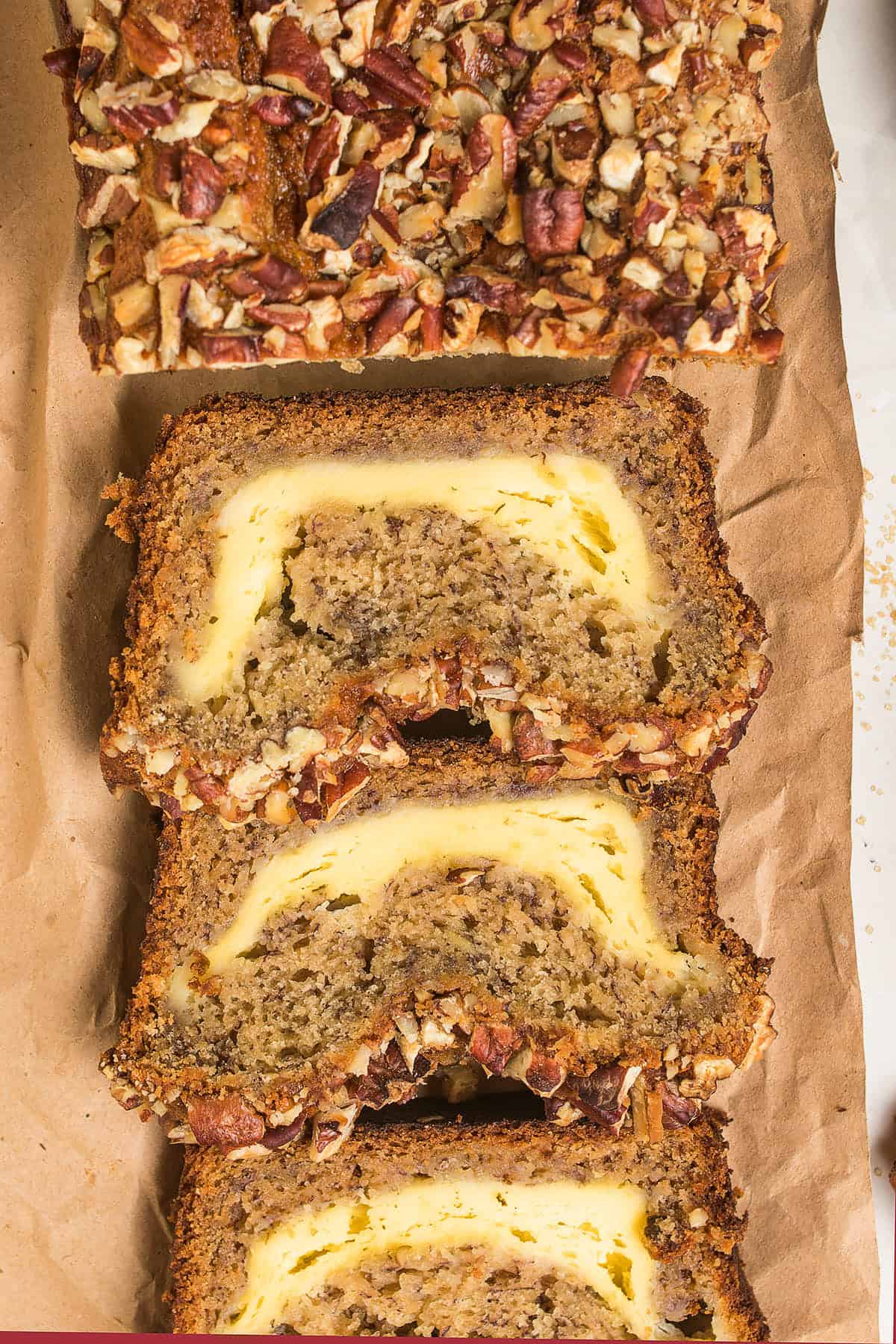 Sliced banana bread with a cream cheese filling and chopped pecans on top, displayed on brown parchment paper, reminiscent of the rustic charm of Dutch Oven Bread.