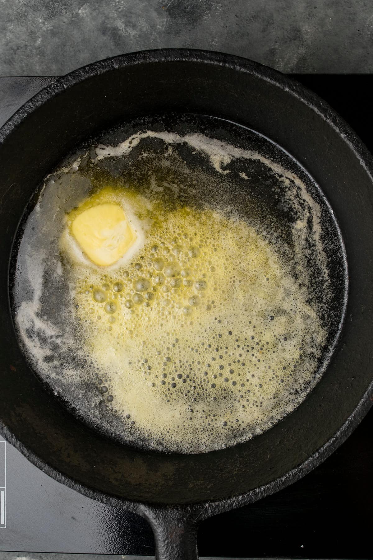 A pat of butter melting and bubbling in a black cast iron skillet on a stovetop, ready to complement slices of fresh Dutch Oven Bread.